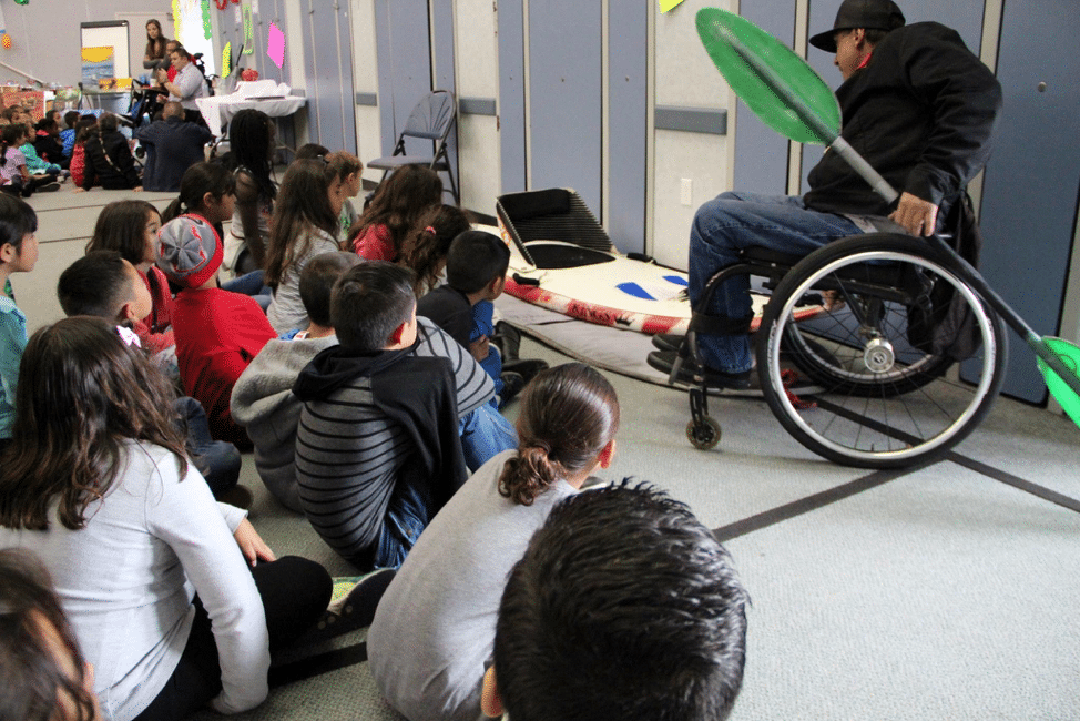 Man in wheelchair showing children in classroom kayak oar