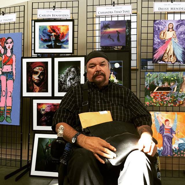 Carlos sitting in front of a wall of his and other people's artwork