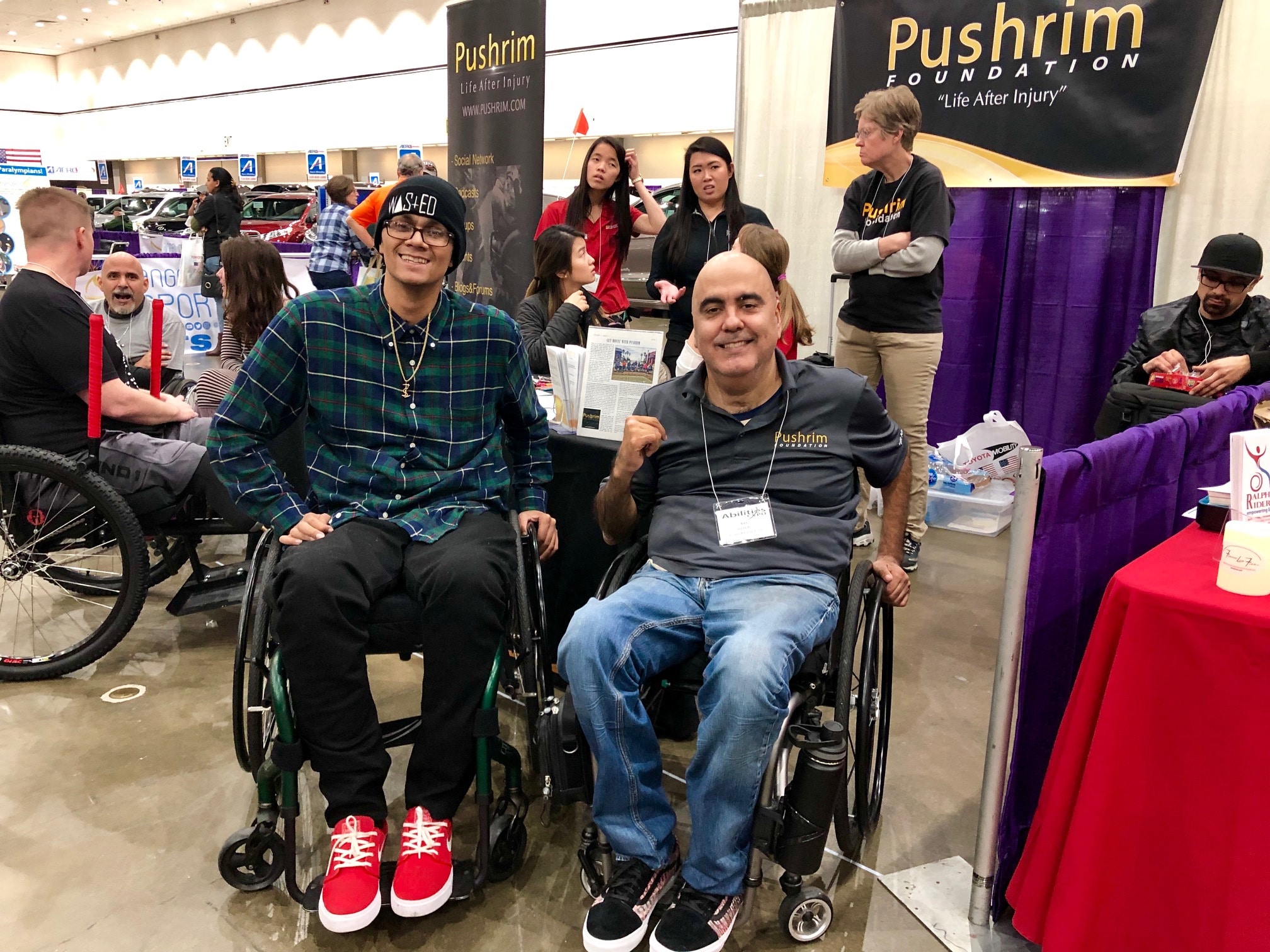 A young main in a wheelchair next to Ray Pizarro in his wheelchair at an expo