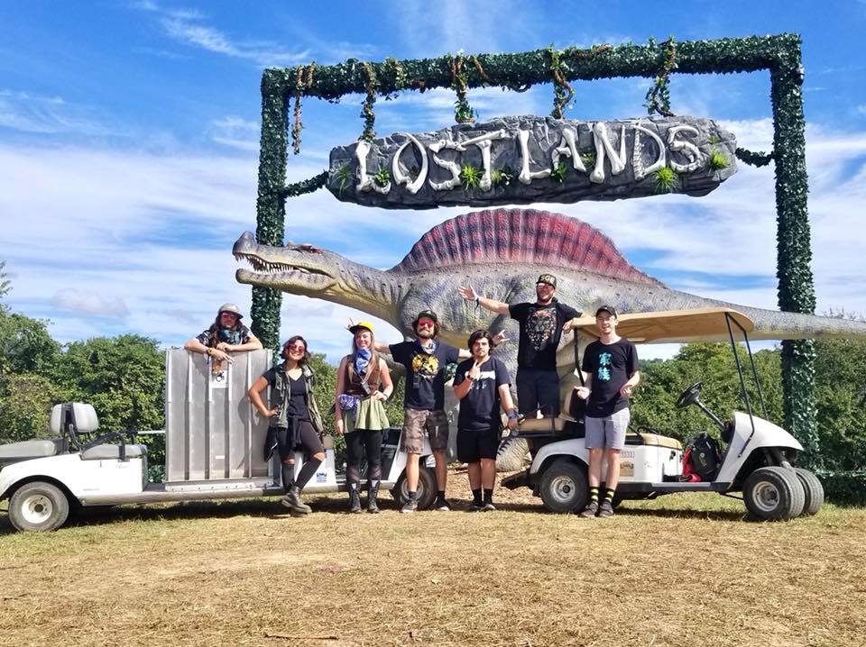 Accessible Festivals crew with golf carts in front of Lostlands sign with a dinosaur statue