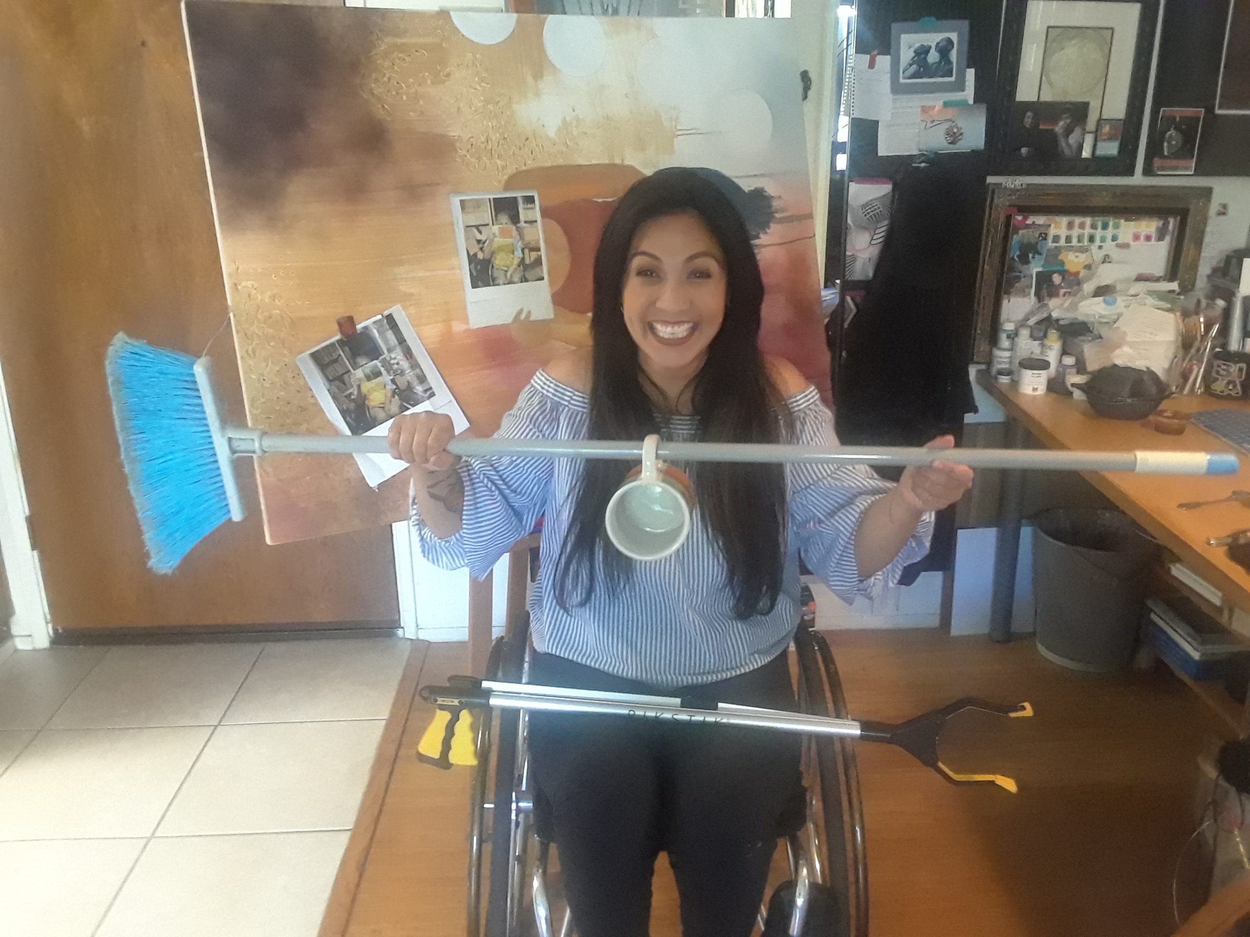 Hydred Makabali in her wheelchair holding a broom with a mug hanging from the stick.