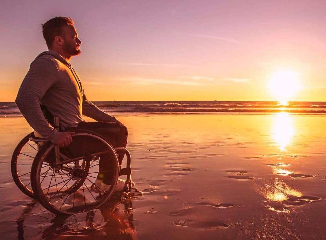 Richard Corbett is sitting in his chair on the shore of a beach. The sun is setting in the horizon.