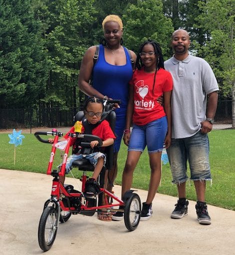 A young girl with her red Freedom Concepts adaptive bike. Her parents and sister are standing behind her.