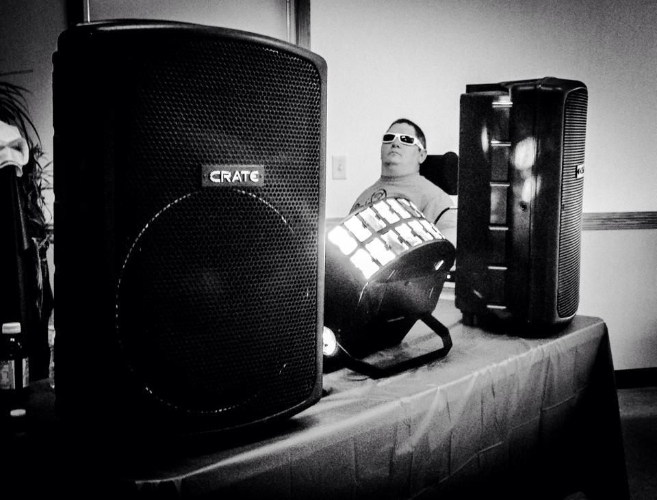 Tim Taylor sits between two large black speakers while he DJs.