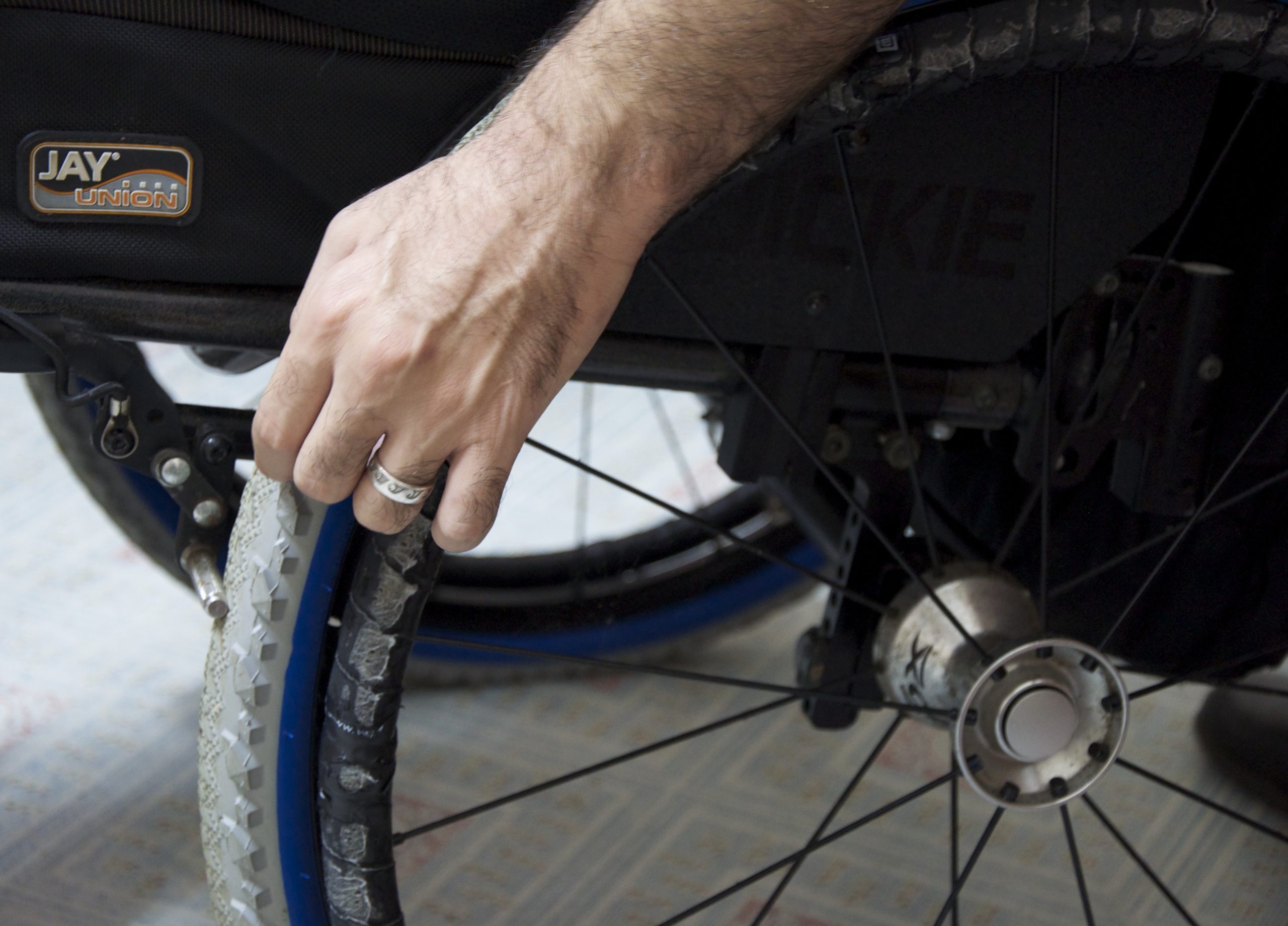 Minna's hand with wedding band on wheelchair wheel.