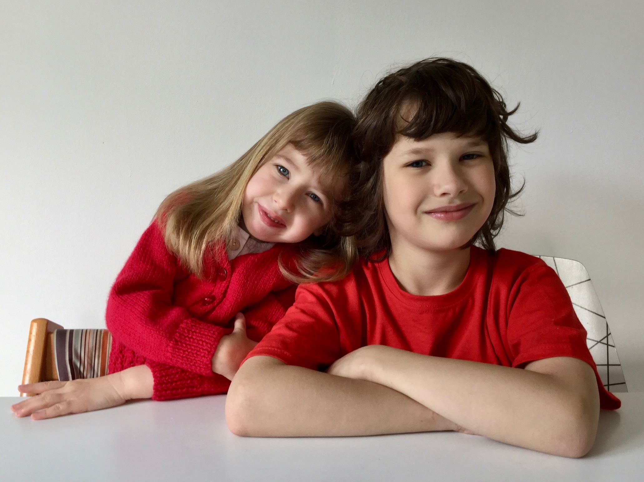Eudora, a little girl with dirty blond hair wearing a read sweater, rests her head on her brother's shoulder, a boy with wispy dark brown hair wearing a read t-shirt.