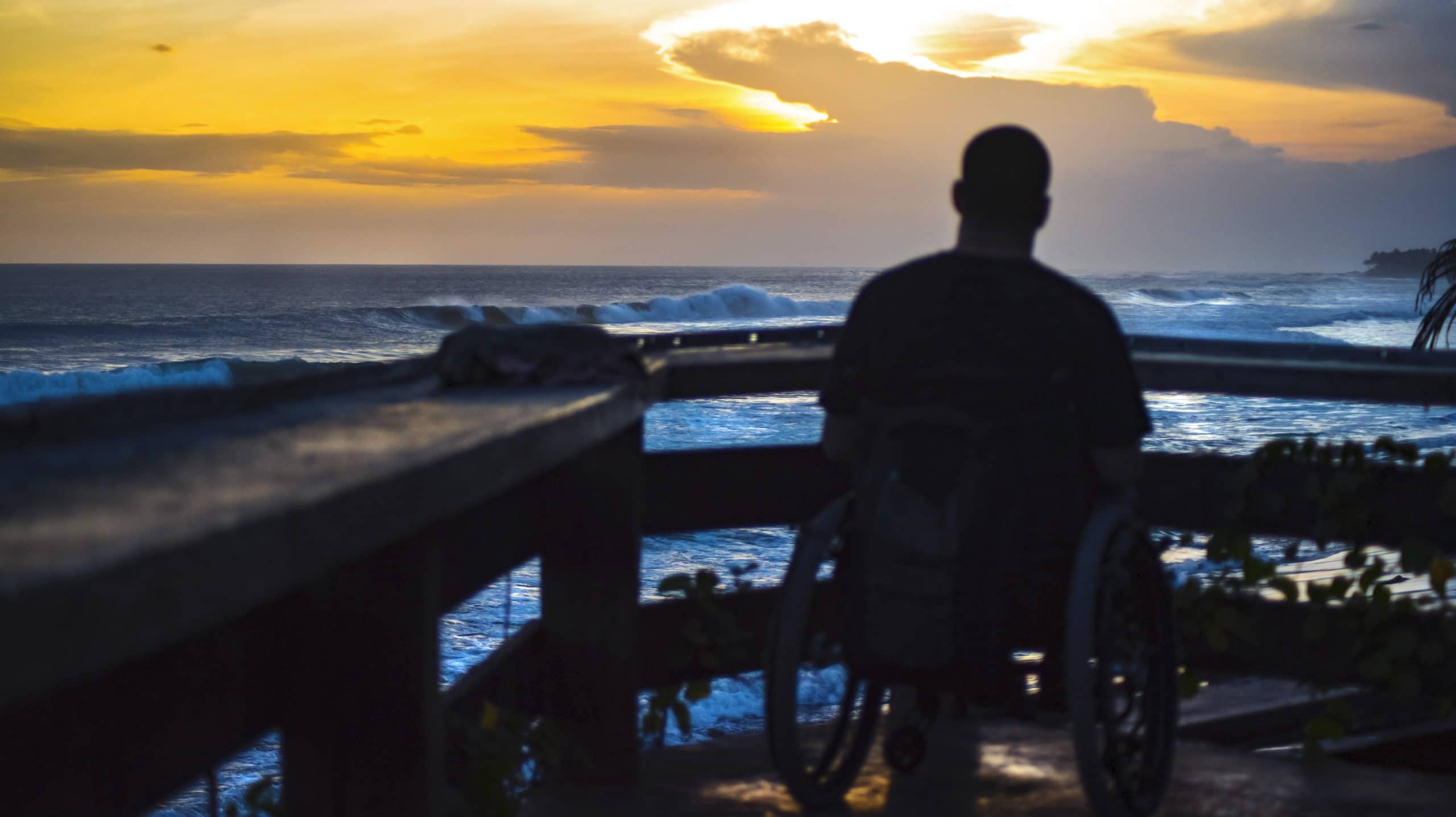 Damien Minna's shadow, sitting on a dock looking out to the ocean at sunset