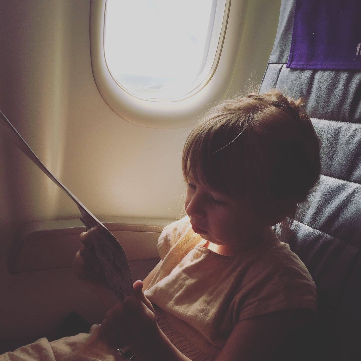 A little girl, Eudora, sits in a window seat on an airplane.