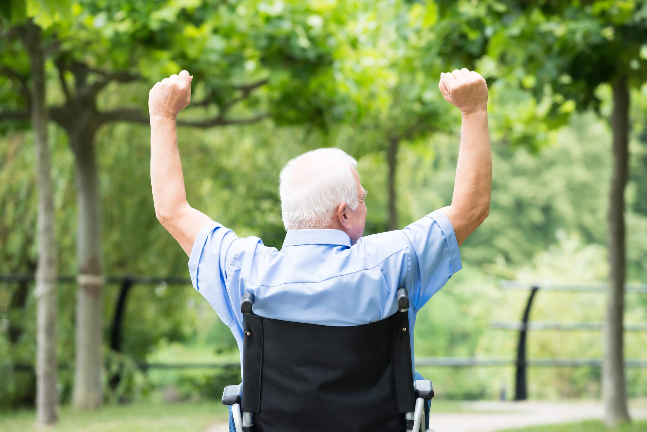 Rear view of a senior man in a wheelchair raising his arms.