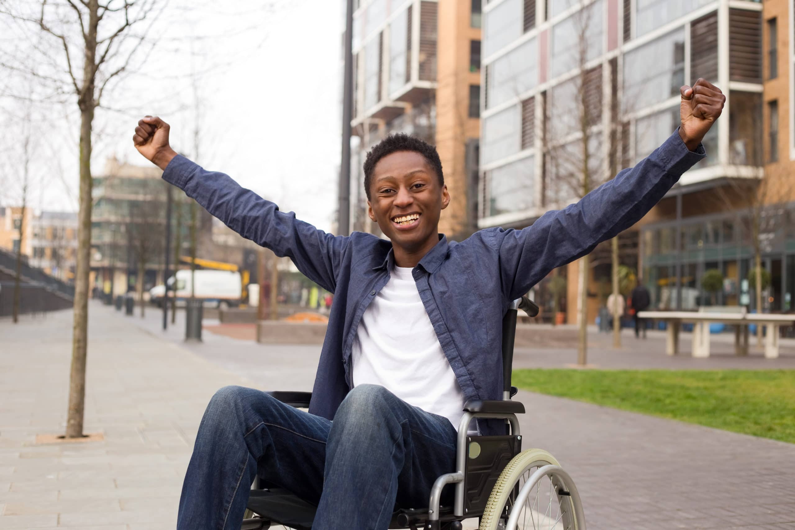 A young man in a wheelchair smiles and holds his arms out.