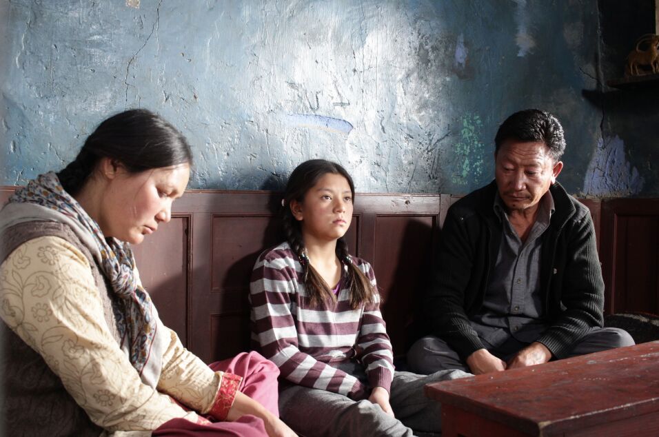 A little girl sits between a man and a woman on a bench.