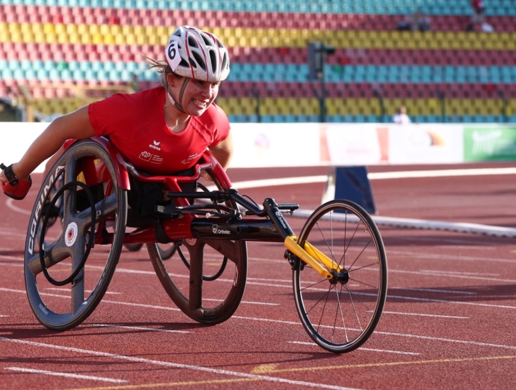 Tanja in a racing wheelchair on an outdoor track. Her arms are back and she's gritting her teeth as if she's pushing hard.