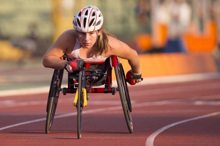 Tanja racing toward the camera on an outdoor track in a racing wheelchair.