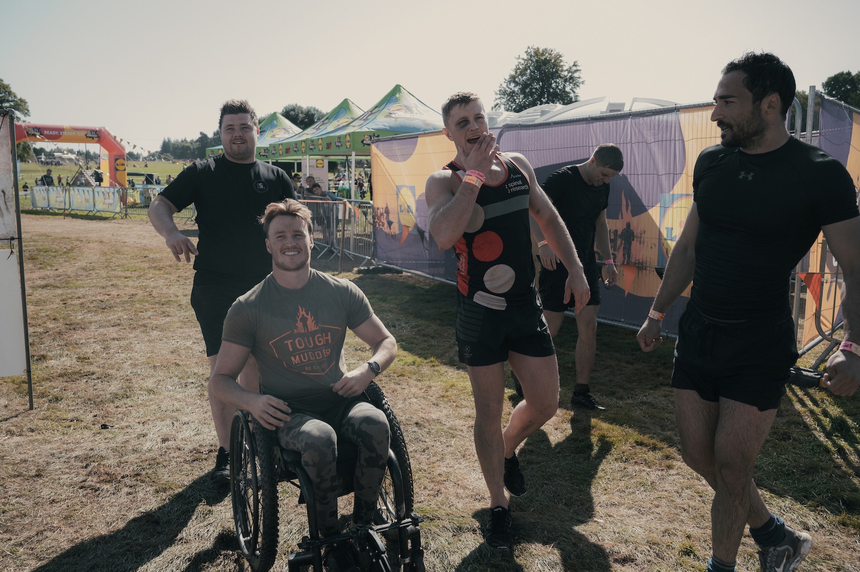 Josh in his wheelchair with four other young men standing around him at a Tough Mudder competition.