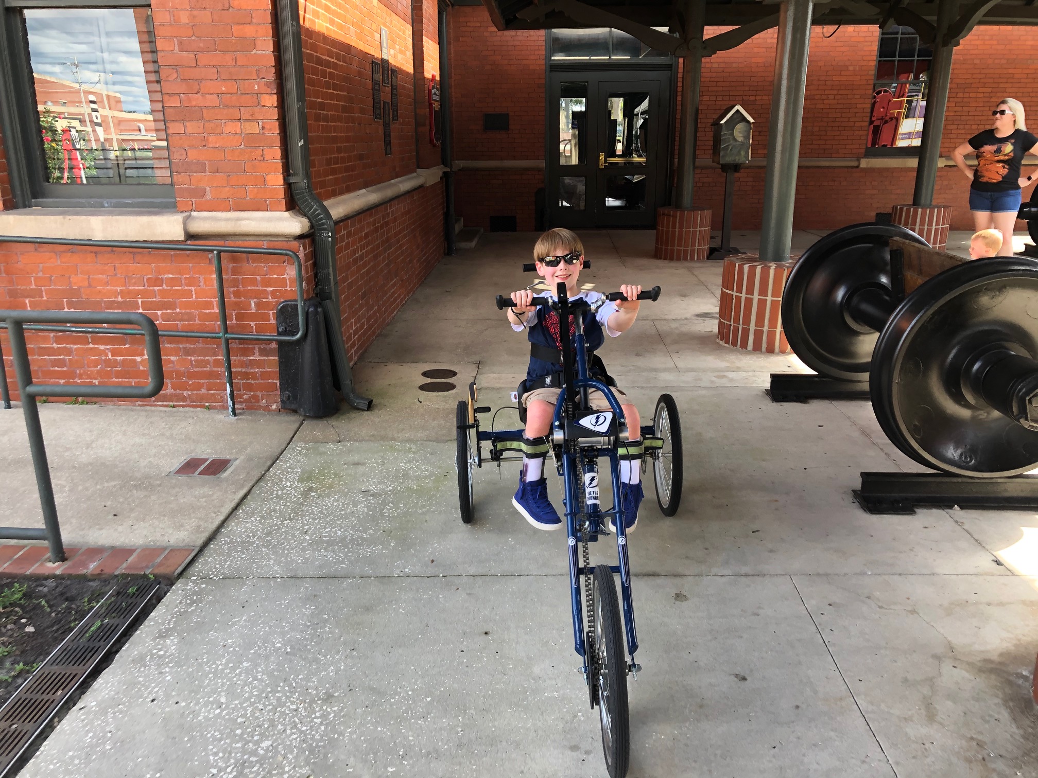 A 9-year-old boy wearing sunglasses riding a three-wheeled handcycle toward the camera.