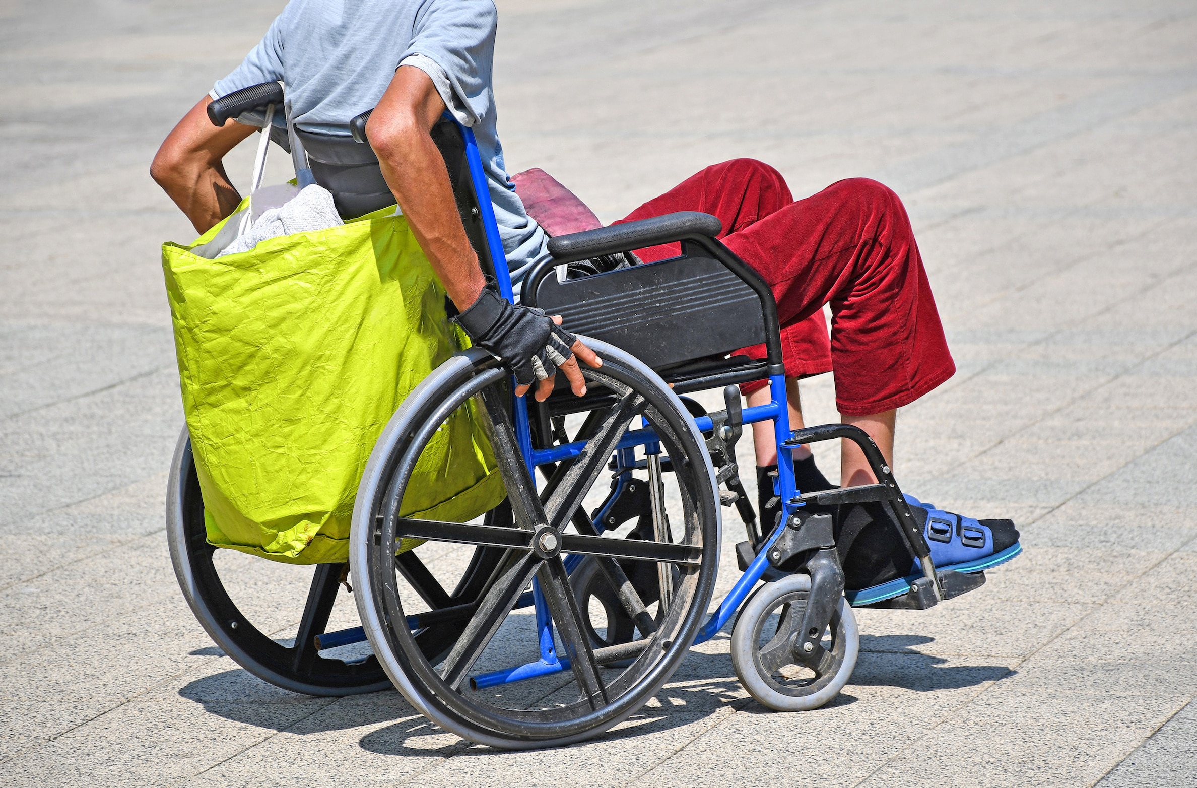 A person in a wheelchair with a reusable shopping bag hooked onto the back.