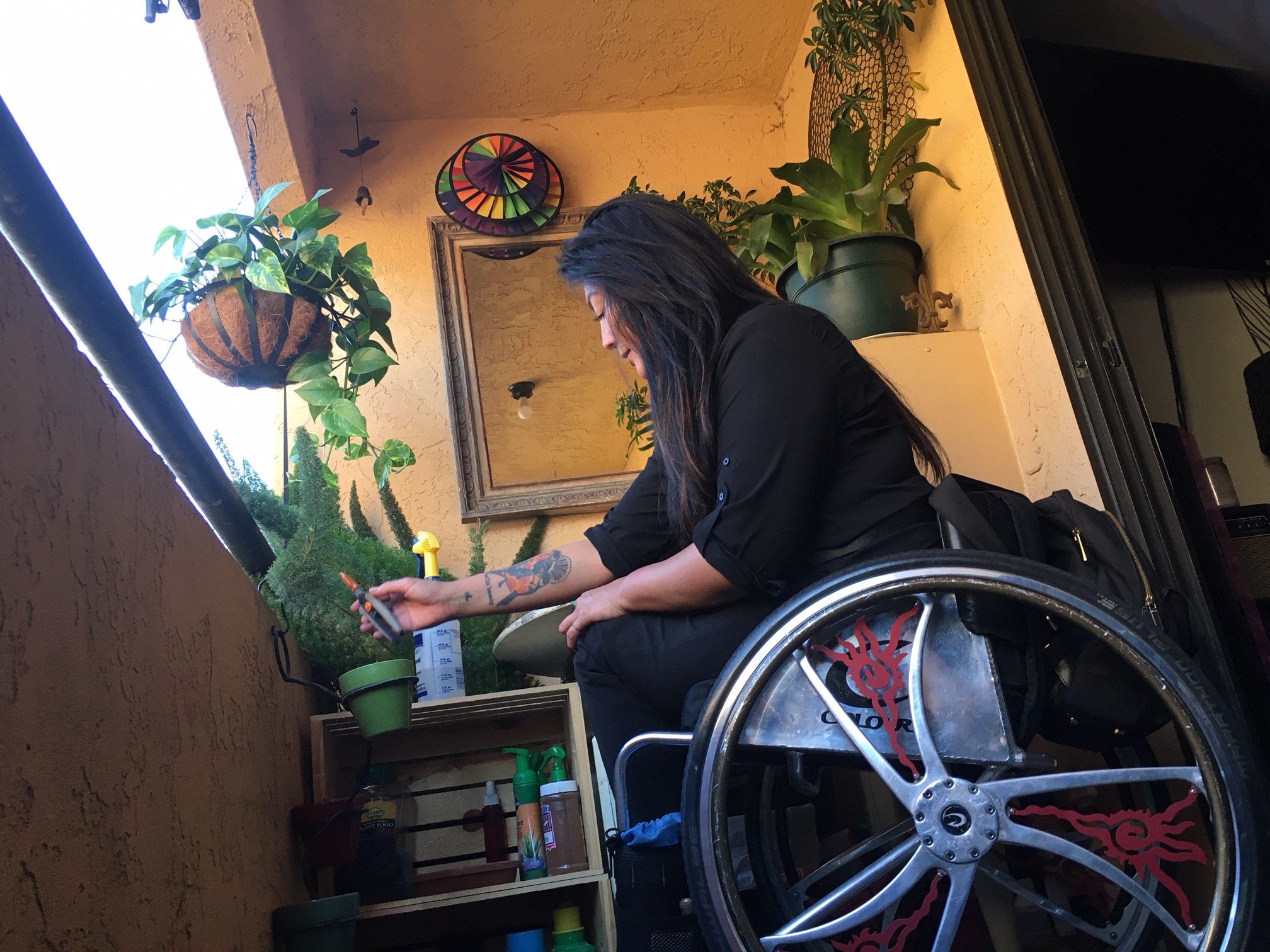 Side view of Hydred Makabali in her Colors wheelchair tending to her plants on her balcony.