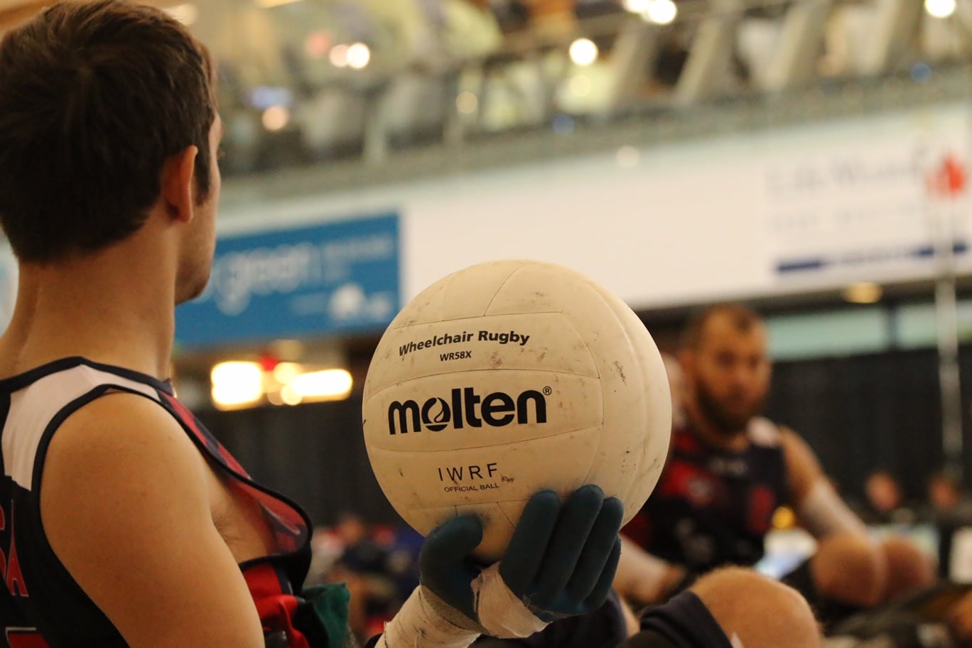 A profile view of Butler from the chest up holding a Molten volleyball that says, "Wheelchair Rugby" and "IWRF Official Ball."