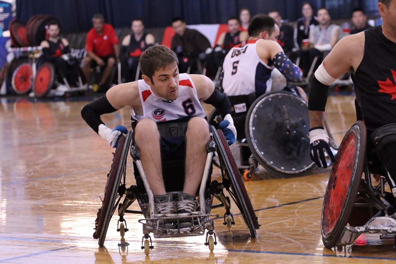 Jeff Butler wheels forward on a gym court in his rugby wheelchair. Other players are in the background. 