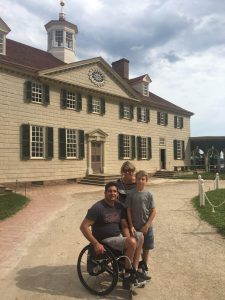 The Orefice family (Anthony, his son, and wife) on a gravel path with a large, white-brick building in the background.