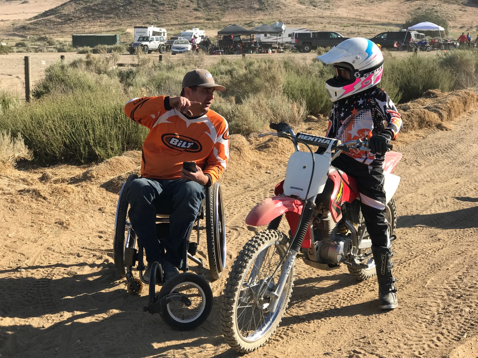 Anthony Orefice in his wheelchair talks to a boy on a dirt bike.