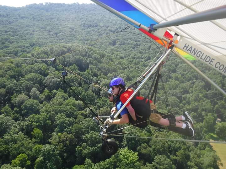 Blakely hang glides in tandem with a pilot over green, forest landscape.