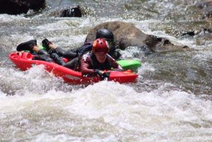 Blakely rides a bellyak down a river with rapids.