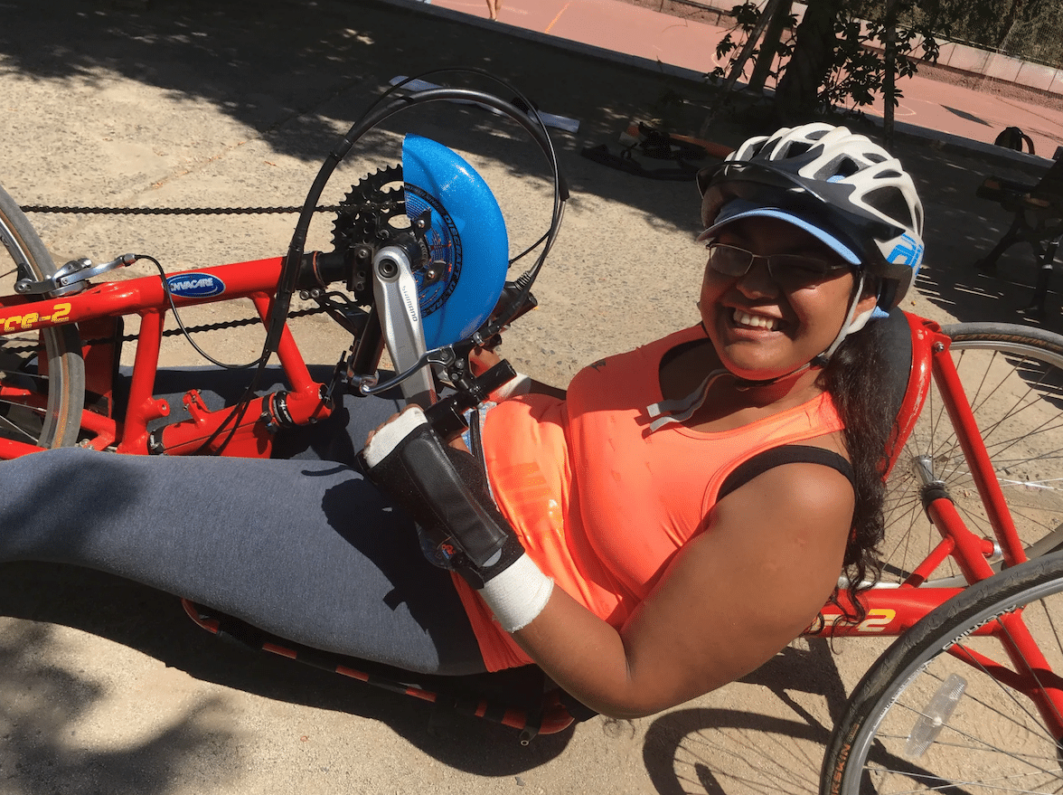 A young woman on a recumbent handcycle. She is smiling at the camera.