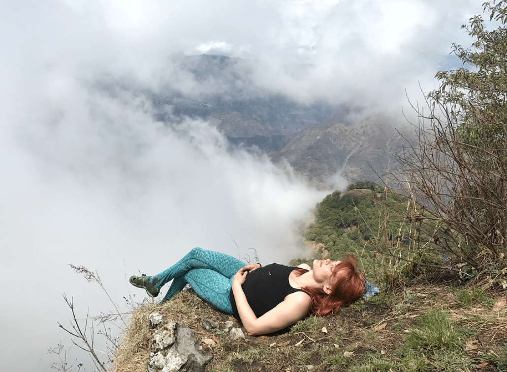 Erin Clark lies on the edge of a cliff. She is surrounded by clouds, but the sun is shining on her.