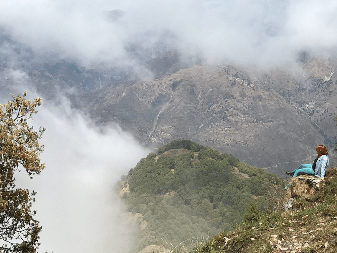 Clark sitting on a green cliff looking out over the mountains and clouds.