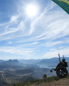 Clark's front, third-wheel attachment of her wheelchair is in the air as she begins to be lifted off the mountain by her paragliding sail.