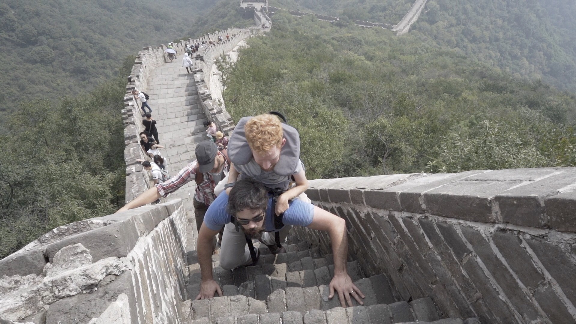 Kevan is being carried by his friend on a very steep section of the Great Wall of China.